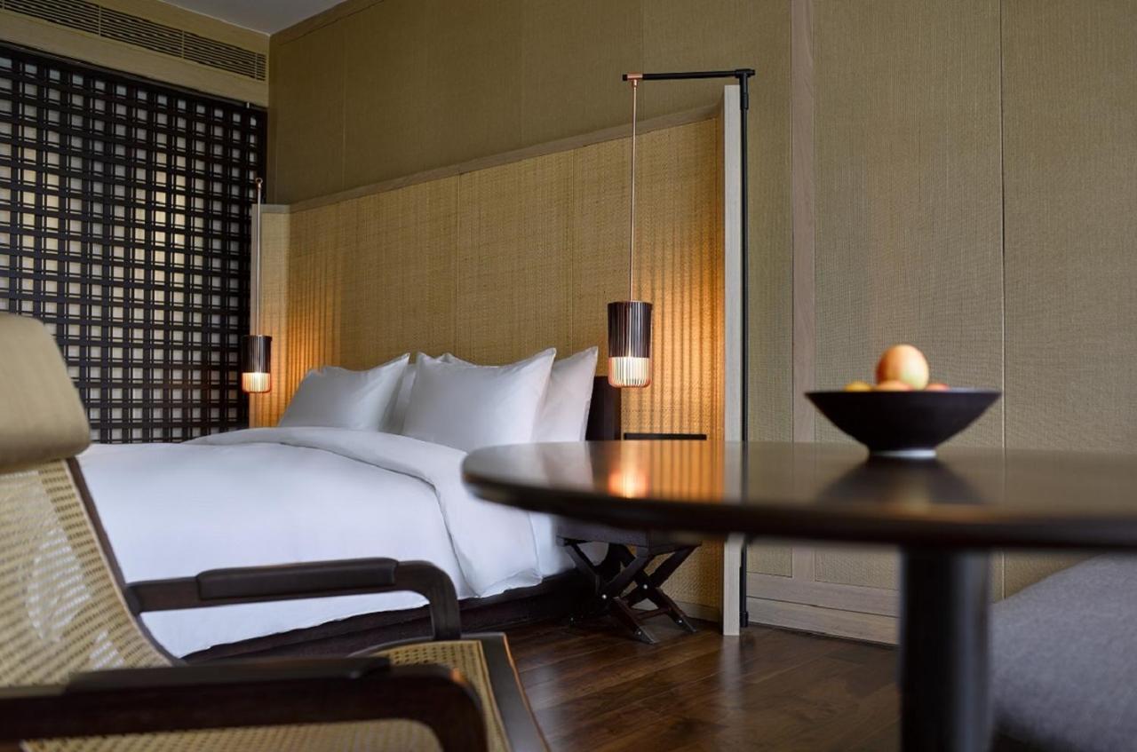 The Ruma Hotel And Residences Kuala Lumpur Exteriér fotografie The photo shows a well-designed bedroom with a modern and minimalist aesthetic. The room features a large bed with white linens, positioned against a textured wall. On either side of the bed, there are pendant lights that provide a warm glow. The dec