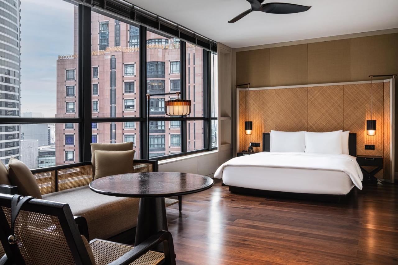 The Ruma Hotel And Residences Kuala Lumpur Exteriér fotografie The photo shows a modern hotel room featuring a large bed with white linens, situated against a backdrop of large windows that allow for ample natural light. The room includes a wooden floor and has a minimalist aesthetic, with a round table and two 