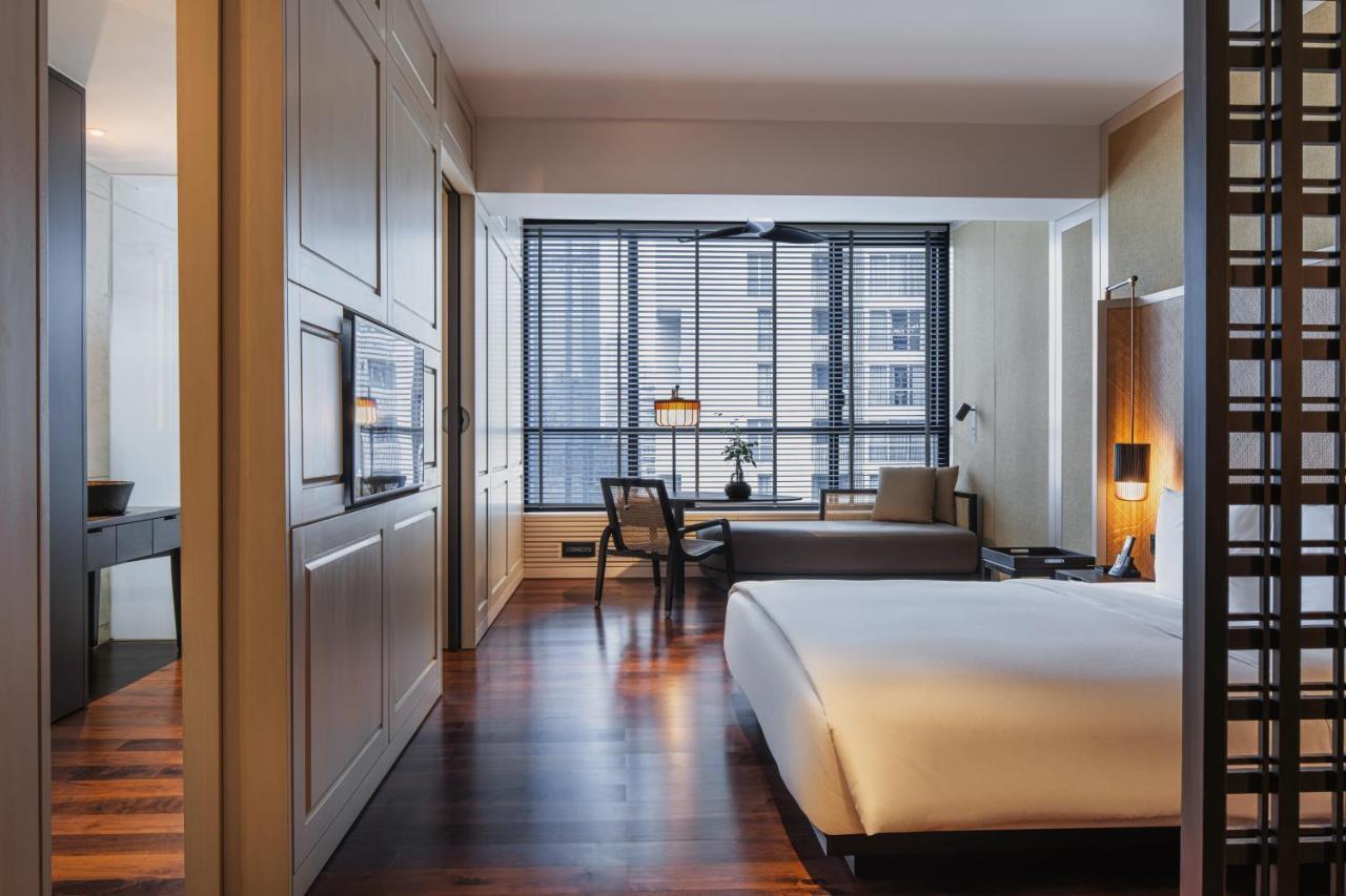 The Ruma Hotel And Residences Kuala Lumpur Exteriér fotografie The photo shows a modern hotel room with a clean and minimalist design. The room features a large bed with white bedding positioned against a wall. There is a wooden floor that adds warmth to the space. A sitting area is visible in the background, fe