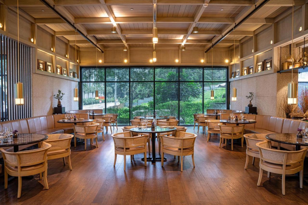 The Ruma Hotel And Residences Kuala Lumpur Exteriér fotografie The photo shows the interior of a modern restaurant. It features wooden flooring, large windows that let in natural light, and an open layout. The seating consists of round tables surrounded by chairs, along with some cushioned booths. The decor has 