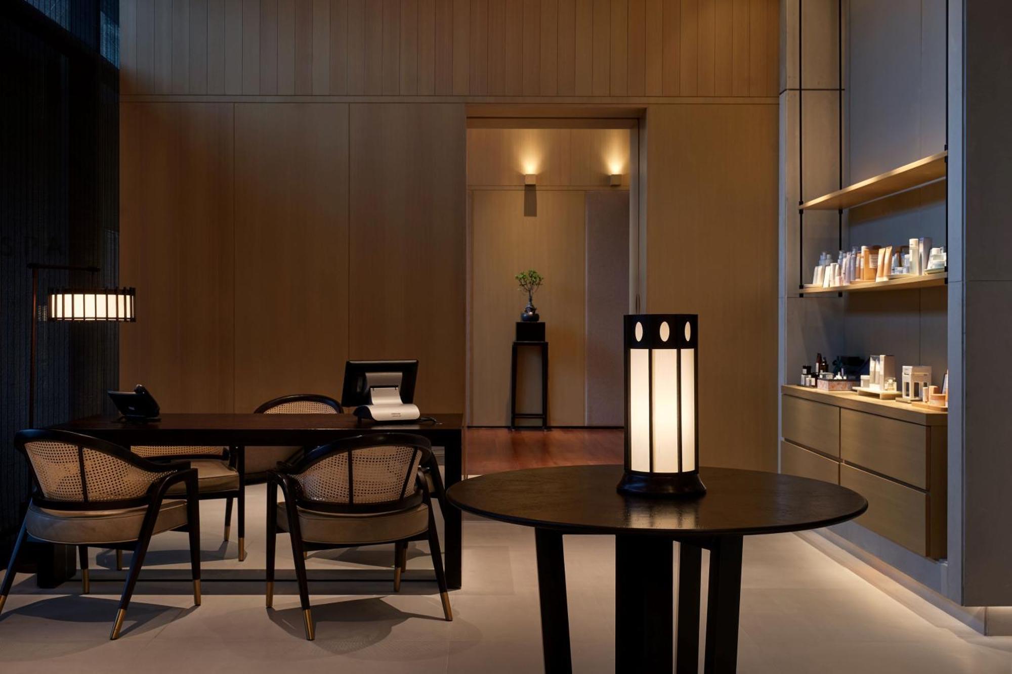 The Ruma Hotel And Residences Kuala Lumpur Exteriér fotografie The photo shows a modern, minimalist interior space. It features a wooden wall with soft lighting, enhancing a calm atmosphere. In the foreground, there is a round table with a uniquely designed lamp on it. Surrounding the table, there are stylish wo